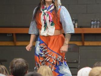 A woman dressed in an orange native american cultural dress with her eyes closed. 